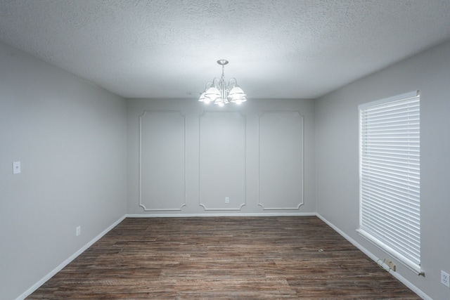 unfurnished dining area featuring baseboards, dark wood-style floors, a textured ceiling, and a notable chandelier