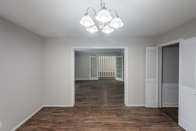 unfurnished dining area with baseboards, a notable chandelier, and dark wood-type flooring