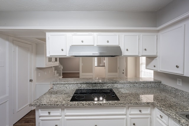 kitchen with dark wood-style flooring, black electric stovetop, white cabinets, and wall chimney range hood