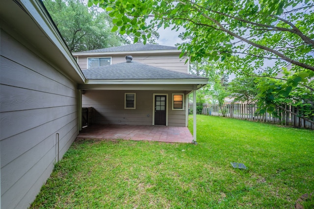 rear view of house featuring fence, a patio, a lawn, and roof with shingles