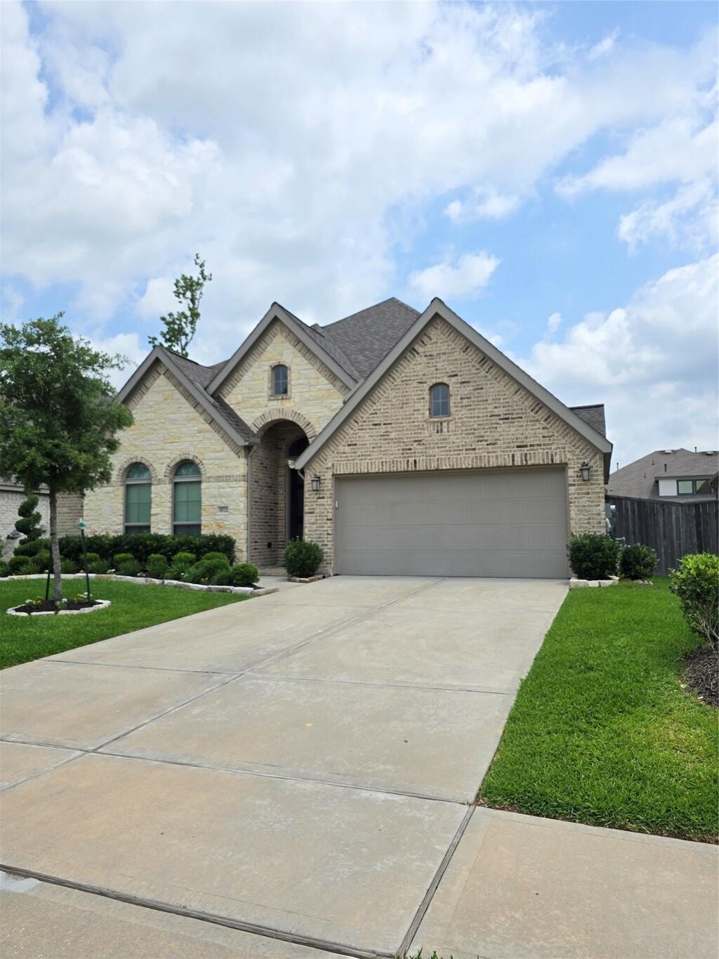 french country inspired facade with fence, brick siding, a garage, a front yard, and concrete driveway