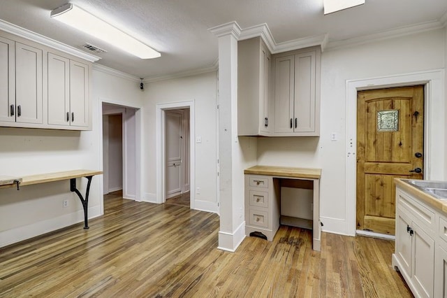 kitchen with crown molding, light wood finished floors, baseboards, and visible vents