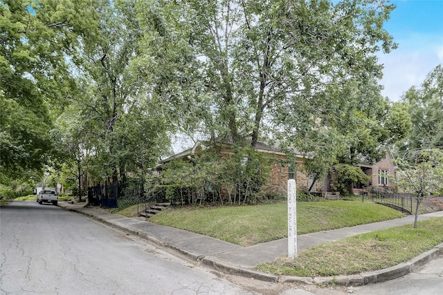 view of property hidden behind natural elements with brick siding, fence, and a front lawn