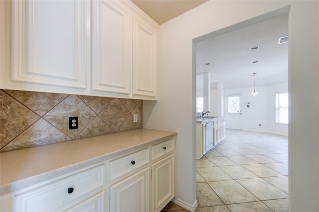 kitchen with backsplash, white dishwasher, a sink, light countertops, and light tile patterned floors