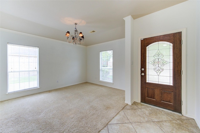 foyer entrance featuring light tile patterned flooring, light colored carpet, a chandelier, baseboards, and ornamental molding