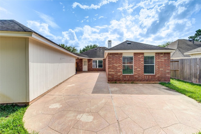 rear view of house with brick siding, fence, a patio, and roof with shingles