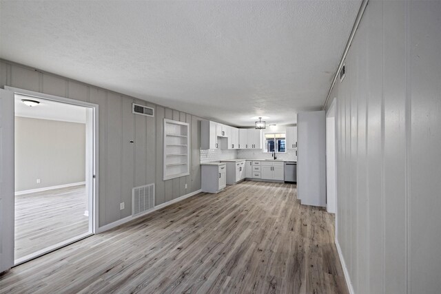 unfurnished living room with an inviting chandelier, a textured ceiling, light wood-style flooring, and visible vents