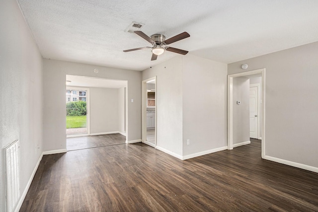 spare room featuring baseboards, ceiling fan, dark wood finished floors, and visible vents