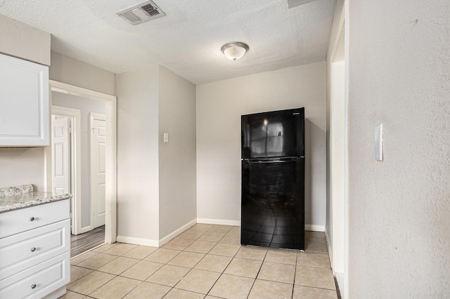 kitchen featuring visible vents, freestanding refrigerator, a textured ceiling, white cabinets, and light tile patterned floors