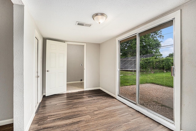 interior space with baseboards, a textured wall, wood finished floors, and visible vents