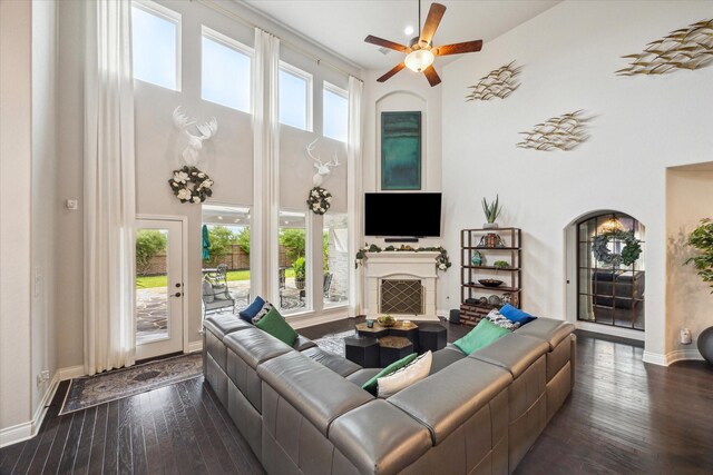 living area featuring dark wood-style flooring, ceiling fan, a towering ceiling, and a fireplace