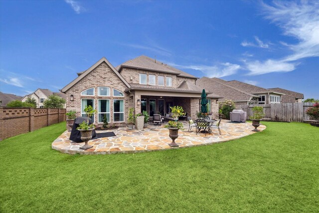 rear view of property featuring roof with shingles, brick siding, a fenced backyard, a lawn, and a patio