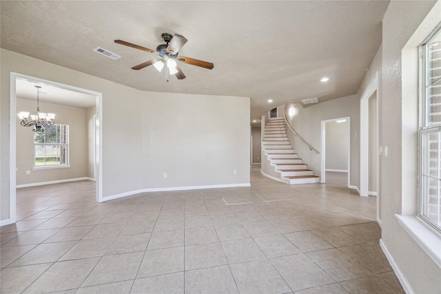 unfurnished room featuring a textured ceiling, visible vents, ceiling fan with notable chandelier, stairs, and light tile patterned flooring