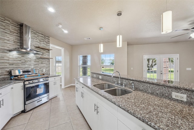 kitchen featuring wall chimney range hood, decorative backsplash, stainless steel gas range oven, a sink, and white cabinetry