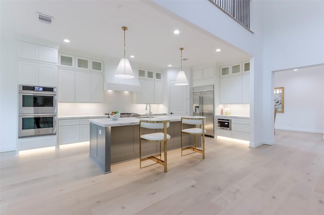 kitchen featuring a kitchen island with sink, stainless steel appliances, visible vents, and white cabinetry