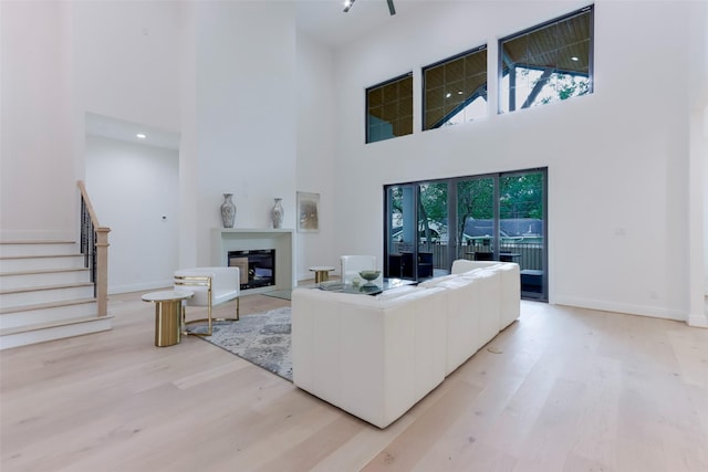 living area featuring light wood-style floors, a glass covered fireplace, a towering ceiling, and stairs