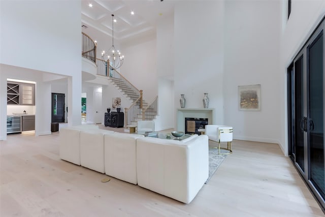 living room featuring beamed ceiling, a high ceiling, coffered ceiling, and light wood-type flooring
