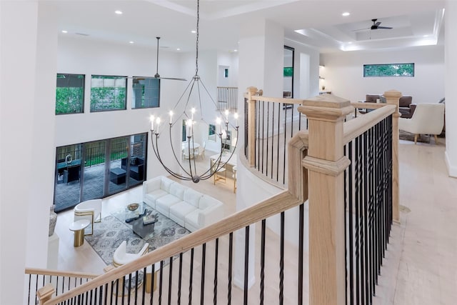 stairway featuring recessed lighting, ceiling fan with notable chandelier, and a tray ceiling