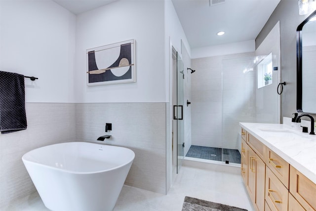full bathroom featuring vanity, wainscoting, tile walls, a freestanding bath, and a stall shower