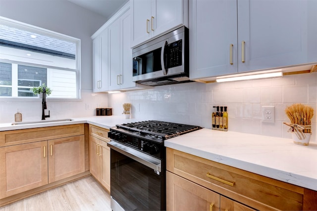 kitchen featuring decorative backsplash, stainless steel microwave, a sink, light wood-style flooring, and gas stove