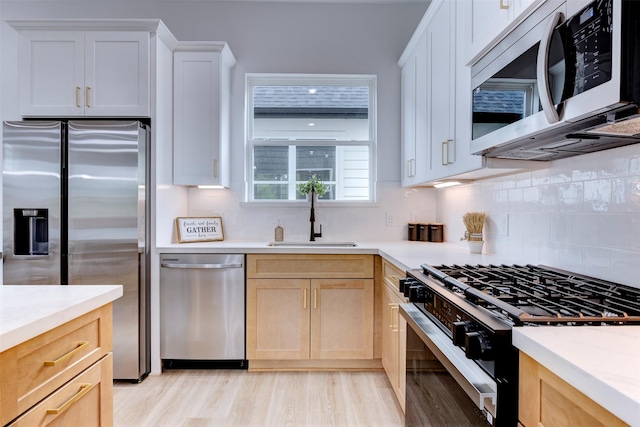 kitchen featuring light countertops, appliances with stainless steel finishes, a sink, and tasteful backsplash