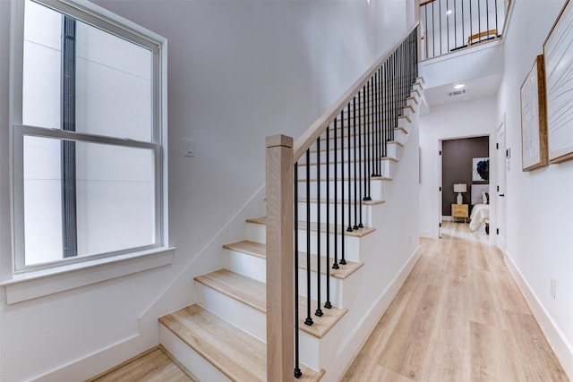 stairway featuring visible vents, baseboards, a towering ceiling, and wood finished floors