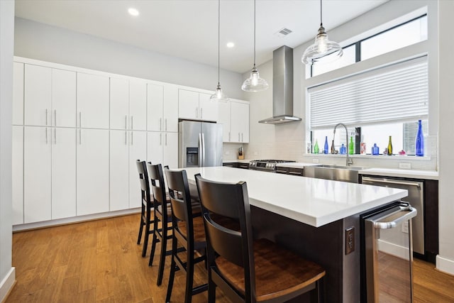 kitchen featuring beverage cooler, a breakfast bar area, wall chimney range hood, a sink, and stainless steel appliances