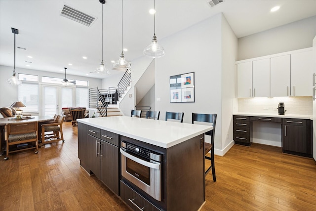 kitchen with a kitchen bar, visible vents, white cabinets, hardwood / wood-style floors, and oven