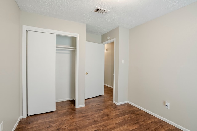 unfurnished bedroom featuring a textured ceiling, baseboards, wood finished floors, visible vents, and a closet