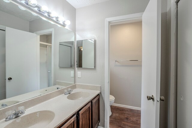 bathroom with a sink, double vanity, toilet, and wood finished floors
