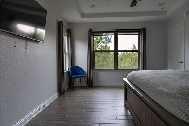 bedroom with ceiling fan, a tray ceiling, dark wood finished floors, and baseboards