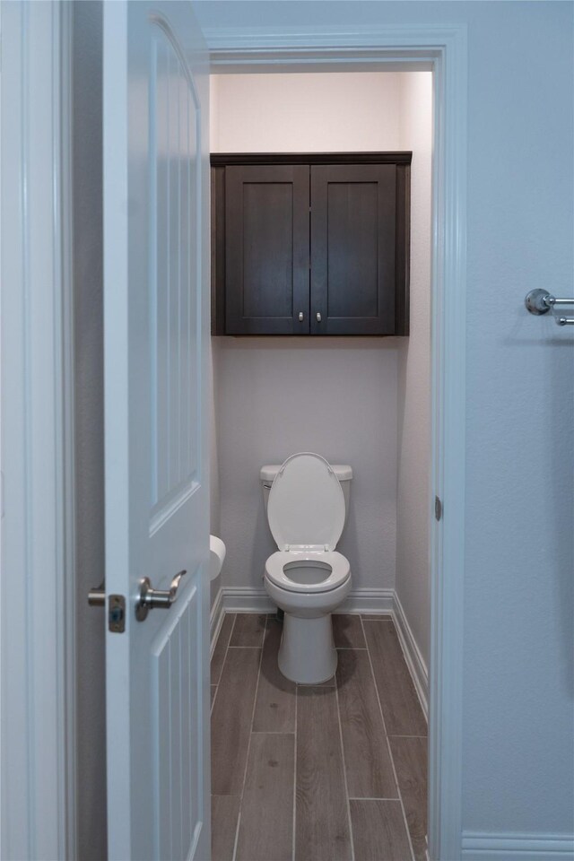 bathroom with baseboards, wood finish floors, and toilet