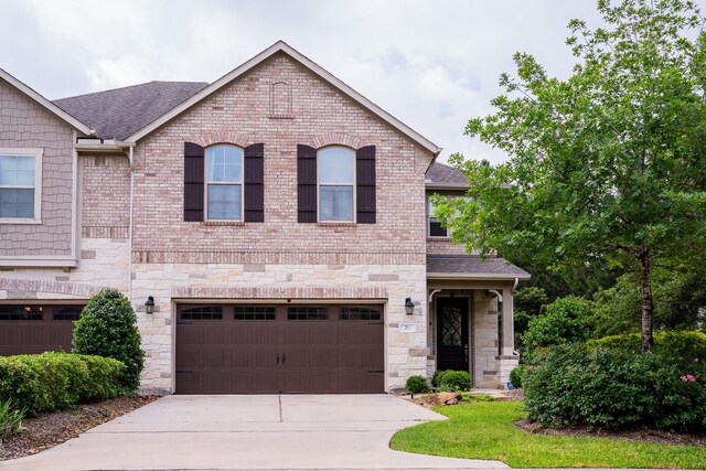 view of front of home featuring a garage, stone siding, roof with shingles, brick siding, and driveway