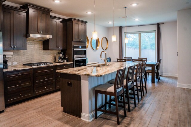kitchen with a kitchen breakfast bar, under cabinet range hood, light wood-style flooring, appliances with stainless steel finishes, and backsplash