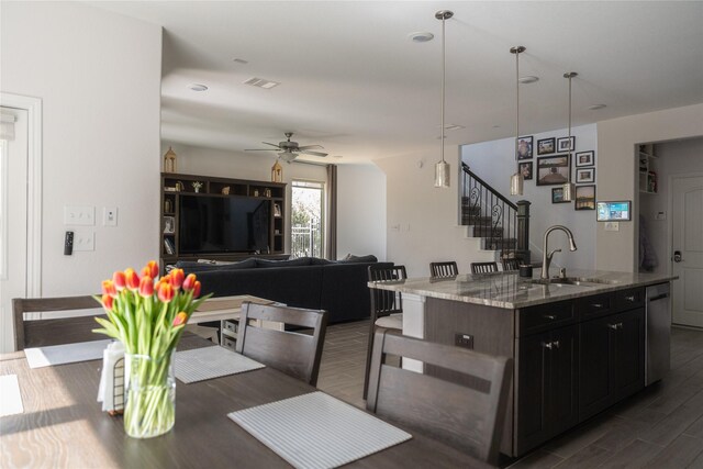 kitchen with dark wood-style flooring, visible vents, light stone countertops, a center island with sink, and a sink