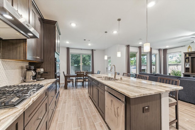 26 Heirloom Garden Pl, Magnolia, TX 77354 - kitchen with a sink, stainless steel appliances, ventilation hood, a breakfast bar, and dark brown cabinetry