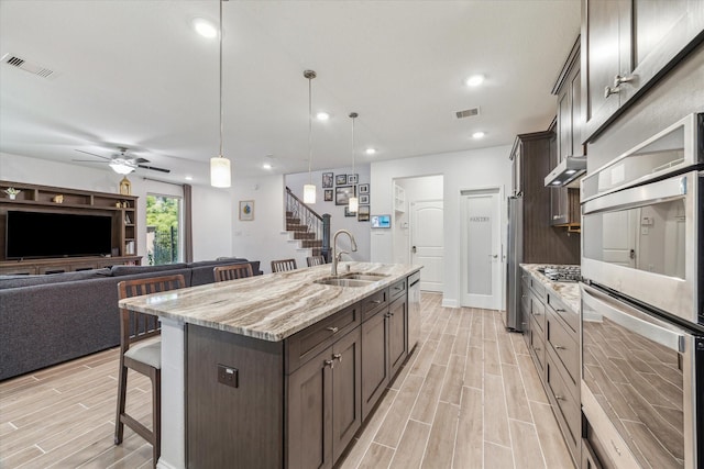 26 Heirloom Garden Pl, Magnolia, TX 77354 - kitchen featuring a sink, a breakfast bar area, stainless steel appliances, dark brown cabinetry, and wood tiled floors