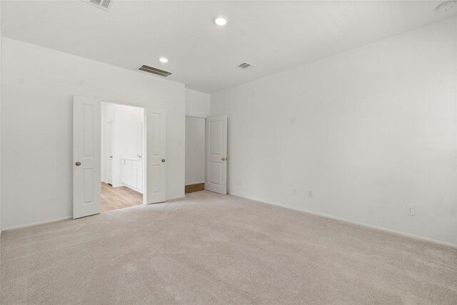 unfurnished bedroom with recessed lighting, light colored carpet, ensuite bathroom, and visible vents