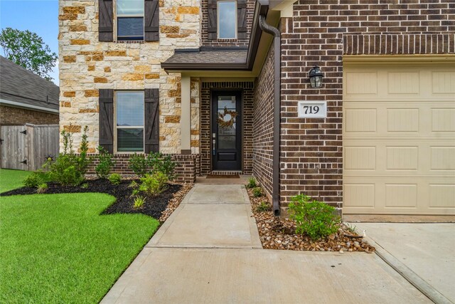 doorway to property with an attached garage, brick siding, fence, and stone siding