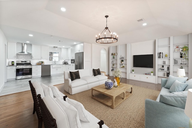 living area with visible vents, light wood-style floors, arched walkways, a notable chandelier, and vaulted ceiling