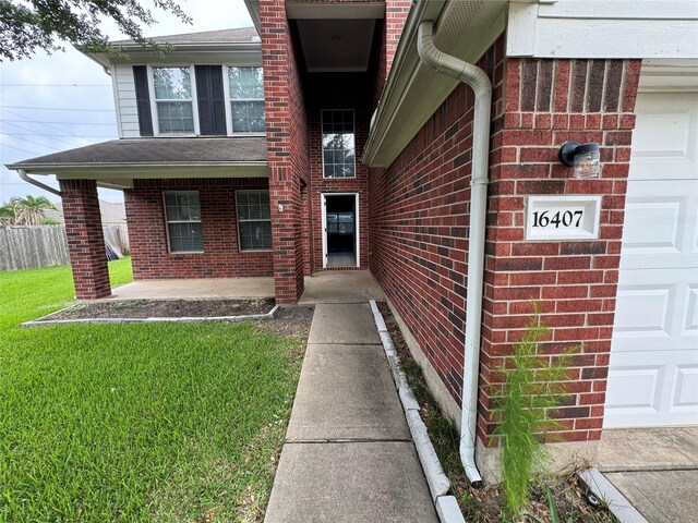 view of exterior entry with a lawn, fence, a garage, and brick siding