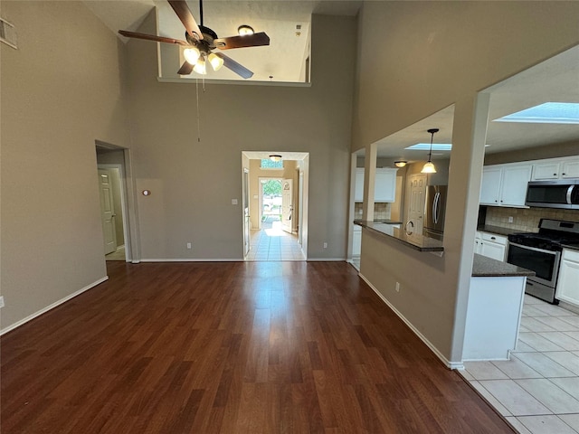 unfurnished living room featuring a ceiling fan, visible vents, wood finished floors, high vaulted ceiling, and baseboards