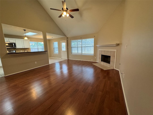 unfurnished living room with a wealth of natural light, a ceiling fan, dark wood-style floors, and high vaulted ceiling