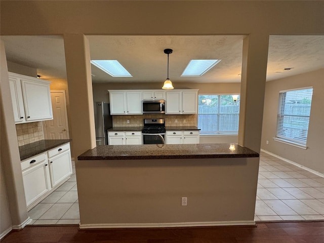 kitchen featuring light tile patterned flooring, white cabinets, backsplash, a skylight, and stainless steel appliances