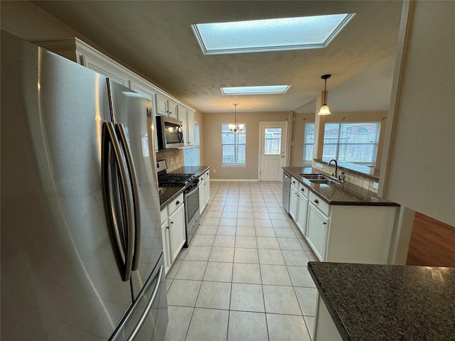kitchen featuring appliances with stainless steel finishes, a sink, a chandelier, decorative backsplash, and a skylight