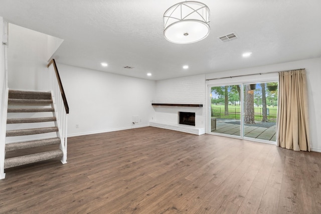 unfurnished living room featuring visible vents, a brick fireplace, stairs, wood finished floors, and recessed lighting