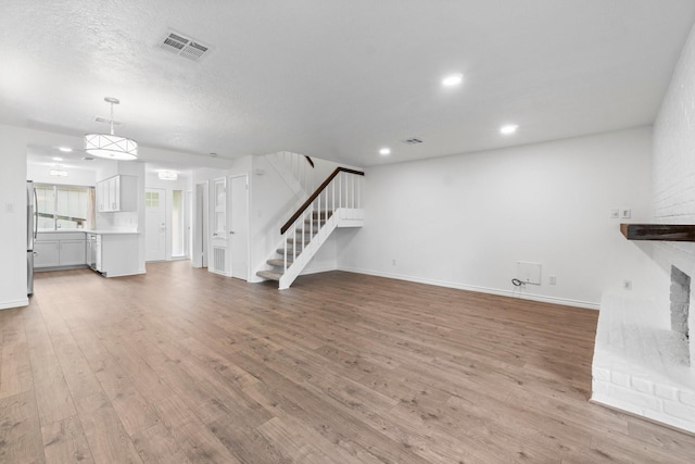 unfurnished living room featuring stairs, baseboards, visible vents, and wood finished floors