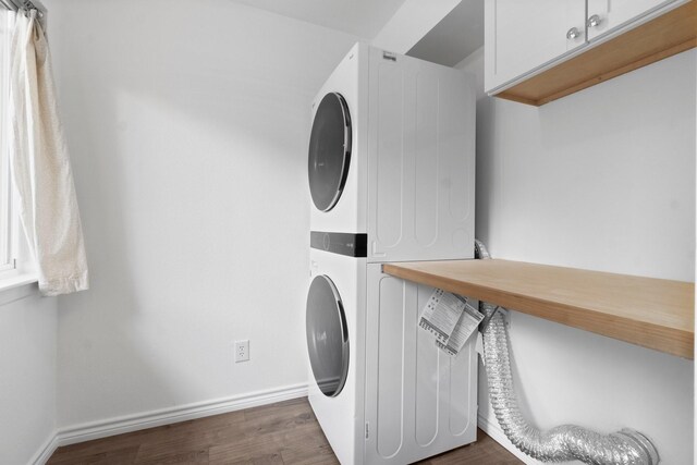 laundry room featuring cabinet space, baseboards, stacked washer and clothes dryer, and dark wood-type flooring