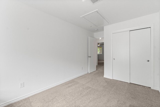 unfurnished bedroom featuring carpet floors, attic access, baseboards, and a closet