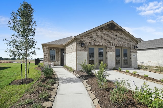 view of front of house featuring brick siding, a shingled roof, french doors, and a front yard